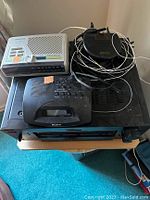 Photo shows white Magnavox alarm clock radio, black Sony alarm clock radio, black Recoton Advent wireless speaker transmitter with cords on top of a black Sony stereo receiver.