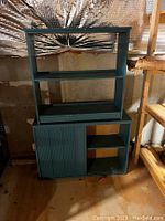 Front view of green storage cabinet showing lower sliding ridged doors and upper open shelving.