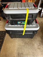 Two Rubbermaid Roughneck storage containers stacked, one large and one smaller, showing their lids and body in used condition in a garage setting.