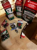 Photo showing two Fluidmaster universal performance toilet fill valves in boxes, one Fluidmaster all-in-one toilet repair kit box, toilet flapper, flexible supply line, and various smaller repair parts on a wooden surface.