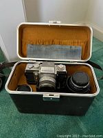 Topcon camera with attached lens and additional lens placed inside metal case with gold interior lining, carrying accessories.