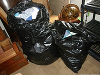 Photo of three large black contractor-size trash bags filled with assorted women's clothing items, bags are full and look heavy.