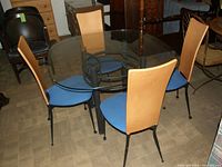 Full view of square glass top table with 4 chairs around it in a room with other furniture.