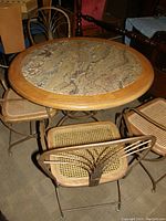 Round wooden table with granite center and five metal/wood chairs with cane seats and decorative backs.