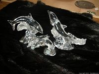 Four Lenox crystal dolphin figurines displayed on black fabric, showing two larger adult dolphins and two smaller baby dolphins with clear, detailed wave bases.