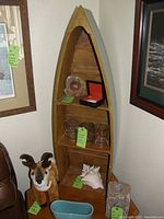 Photo shows a wooden wall shelf shaped like a boat colored gray on the outside and natural wood inside. Includes three shelves. Shelf contains some small decor items (not included). Visible signs of light use wear.