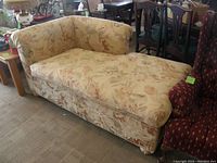 Front and side view of a floral pattern upholstered chaise lounge with a curved backrest and armrest on one side, showcasing the full seating area and fabric design.