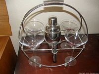 Full set of Harley Davidson martini glasses, metal shaker, and metal stand on wooden surface.