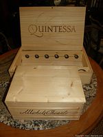 Open Quintessa wooden wine crate showing six internal segmented bottle holders and the lid branded with 'Quintessa'.