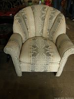 Front view of a lightly used upholstered side chair with a shell-shaped back and padded arms, featuring vertical striped and ornate patterned fabric in beige and gray tones.