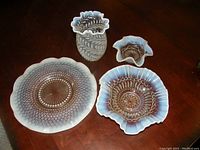 Four pieces of opalescent glassware laid on a wooden table: large oval platter, medium and small ruffled bowls, and a vase.