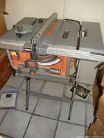 Full view of the Rigid table saw on its stand showing the metal table surface, miter gauge, fence, and power cable.