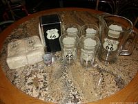 Complete lot of Route 66 branded glassware, napkin holder, and napkins displayed on granite table.
