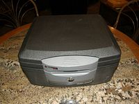 Closed view of the Sentry fireproof and waterproof safe showing textured dark gray outer casing and light gray locking panel with keyhole.