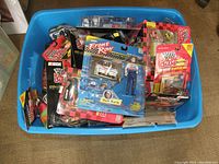 Top-down image of a large blue plastic storage tub filled with new on card NASCAR die cast collectibles. Variety of brands and packaging styles visible, including Racing Champions and Front Row. Packaging conditions vary with possible defects noted.