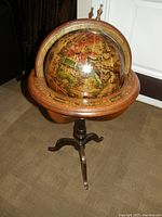Photo of a wooden globe with antique-style map on a three-legged wooden stand, showing detailed map and outer ring markings.