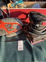 Photo showing two electric sanders, one Black & Decker and one Craftsman, on a table with cords and sandpaper sheets in the background.