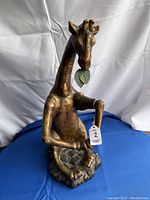 Front view of the full giraffe figurine seated on a base covered in textured leaf-like pattern, showing the posture and overall shape.