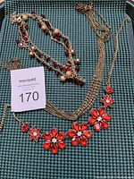 Full view of the three goldtone and red crystal/rhinestone necklaces arranged together on a textured dark surface.
