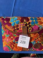 Front close-up of handbag showing colorful floral embroidery and leather flap closure with snap.