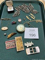 Tray containing assorted vintage jewelry pieces including belt buckle, brooches, earrings, pendants, pins, and tie tack.