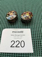 Two enameled oval metal pill box pendants shown side-by-side, highlighting size and shape.