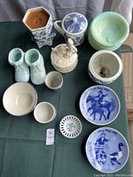 Photo showing a variety of blue and white ceramics including a dresser box with lady, lidded jar, small shoes, cups, bowls, and two blue and white Mothers Day plates.