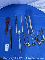 Group photo of 7 letter openers and 6 small decorative spoons on blue background