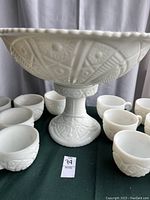 Side view of milk glass punch bowl on pedestal with hobstar and ladder pattern, surrounded by cups.