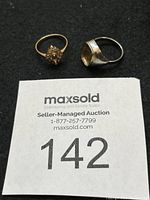 Photo of two rings - a gold floral ring with stones and a silver ring with concave bezel, displayed on black background with auction lot number tag.