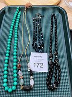 Photo of the full jewelry lot on a black textured surface containing turquoise bead necklace, polished stone necklace, black faceted bead necklace, and black bead bracelet.