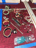 Photo showing a variety of costume jewelry arranged on a red surface, including bracelets, rings, brooch, and necklaces