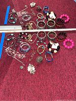 Full lot showing multiple bracelets, rings, chains, and pin on a red carpet background.