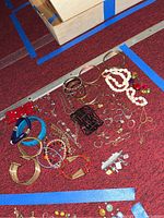 Photo showing assortment of costume rings, bracelets including beaded and metal bangles, also necklaces with beads and charms spread on red carpet