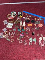 Full display of assorted costume jewelry pieces including earrings, bracelets, pendants, and pins laid out on red fabric.