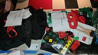 Photo showing folded black costume pieces, red mask with bat wings, boxed vampire fangs and several other costume parts laid out with inventory notes.