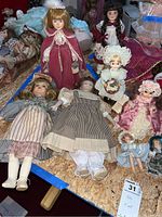 Photo showing a group of eight vintage dolls on a tabletop with period dress and porcelain faces