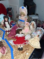 Seven vintage dolls on table, various sizes and styles including porcelain and cloth; some wearing bonnets, lace, and period clothing