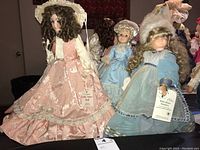 Three collectible porcelain dolls displayed together: Lady Anne Doll in pink dress and hat, Little Queen Guinevere Doll in blue dress with fur bonnet, and Royal Doll limited edition in blue dress with white bonnet.
