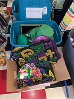 Bin labeled 'St Patrick's Day' containing various green hats, glittery party signs, and other St. Patrick's themed decorations packed in a cardboard box.