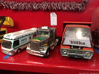 Three vintage toy trucks: Tonka hydraulic truck with rusty cab, Hess Gasoline truck with white body and green stripe, Nylint green and chrome semi truck.