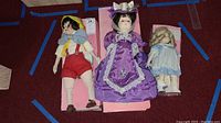 Three vintage porcelain dolls including Pinocchio, Effanbee Age of Elegance, and a smaller doll in light blue dress laid on pink boxes on carpet.