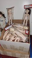 Photo of open box showing many nude porcelain-look plastic dolls inside original plastic packaging