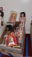 Box containing several vintage plastic dolls of various skin tones and hair colors, some in partial packaging.