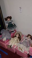 Four vintage dolls seated on pink polka dot boxes against a white wall, showing full-body details and outfits.