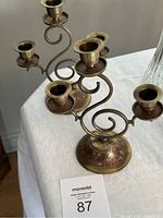 Photo showing one brass candlestick holder with five candle sockets and decorative scroll arms on a white surface.