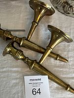 Three heavy brass wall-mounted candlestick holders displayed on a white cloth background with auction lot number 64 card visible.