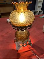Amber glass hobnail lamp illuminated, showing full lamp structure on red cloth.