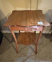 Front view of antique wooden table showing scalloped tabletop edges, carved apron and curved legs with lower shelf.