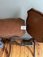 Two antique folding tables with brown leather tops and gold decoration. The tops fold down. Both tables have tripod legs and curved edges.